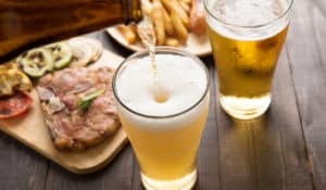The Best Pub Guide - A pint of golden beer is being poured next to another, surrounded by sizzling grilled meats, fresh veg, and crispy chips on a rustic wooden table—the perfect scene for discovering "Gastropubs in the UK – Great Food and Real Ale." Whether you’re seeking top-rated spots or dog-friendly pubs nearby, we’ll help you find your new favourite local!. | Pub Directory UK