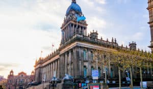 The Best Pub Guide - Leeds: Picture this—a magnificent historic building with stately columns, elegant statues, and a proud clock tower topped by a fluttering blue flag. It’s the sort of architectural gem you’d expect to find gracing the heart of many UK cities (and often spotted near some top-notch local pubs). Stone lions keep watch beside leafless trees, all under a sky that can’t quite decide between sunshine or cloud—classic British weather! Perfect scenery for exploring local watering holes nearby. | Pub Directory UK