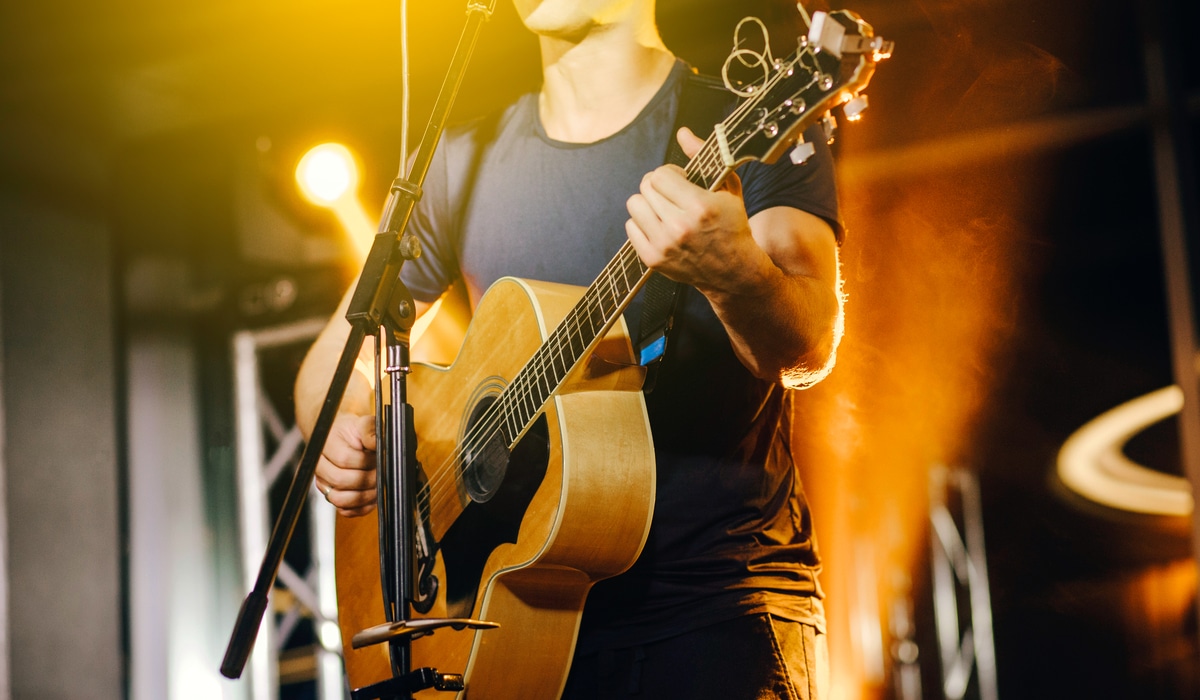 The Best Pub Guide - A gifted musician in a dark shirt strums an acoustic guitar and sings beneath warm yellow lights, perfectly capturing that cosy live music atmosphere you’ll find at venues featured in The Good Pub Guide—your go-to directory for UK pubs with cracking ambience. | Pub Directory UK