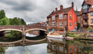 The Best Pub Guide - A charming stone bridge arches over the tranquil river in Norwich, where boats bob gently along the banks and historic pubs and classic brick houses create a welcoming scene. It’s the perfect place to soak up riverside views, discover some cracking local pubs, and explore our UK pub listings for your next great find. | Pub Directory UK