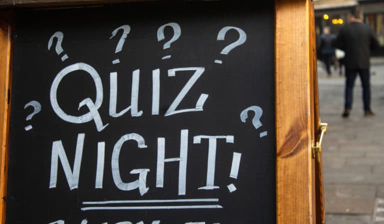 The Best Pub Guide - A blackboard sign outside cheerfully announces "Quiz Night!" framed by playful question marks, as people stroll past—a classic scene you'll spot in our Pub Quiz directory of dog-friendly pubs. | Pub Directory UK