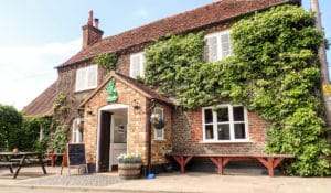 The Best Pub Guide - Step into the Classic British Pub Atmosphere—a welcoming, traditional pub full of charm. Picture a characterful brick exterior draped in ivy, white-framed windows, rustic benches for relaxing pints outside, and a classic hanging sign swinging gently above the door. It’s a true haven for dog lovers and anyone searching for good old-fashioned hospitality! If you’re browsing the latest UK pub listings, put this gem at the top of your must-visit list. | Pub Directory UK