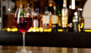 The Best Pub Guide - A glass of red wine sits elegantly on a gleaming bar at Wine Bar in the UK, bathed in warm lighting with shelves of blurred bottles in the background. It’s the perfect setting for a cosy evening—ideal for those who enjoy a relaxed atmosphere, fine wines, and even bringing along their four-legged friends. Discover more inviting dog-friendly pubs just like this using our pub directory!. | Pub Directory UK