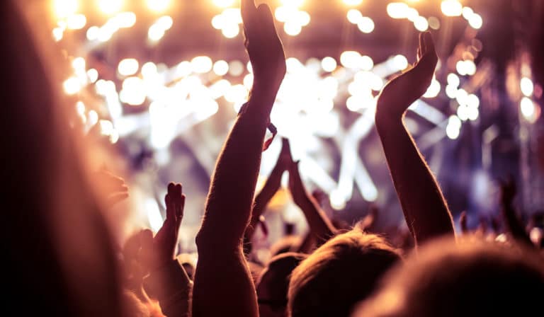 The Best Pub Guide - A buzzing crowd with hands in the air enjoys a concert beneath vibrant stage lights—a spirited scene, just like those unforgettable nights out at your favourite local. Perfect for capturing the energy and excitement that make British pubs so special. | Pub Directory UK
