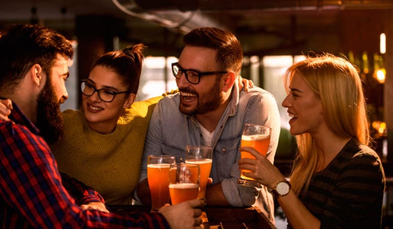 Friends drinking beer at a lively British pub – Find UK pubs near you with The Best Pub Guide
